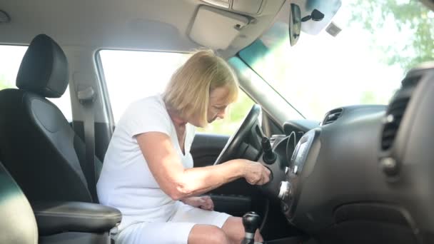 Mujer mayor conduciendo sentada en un coche nuevo, usando cinturones de seguridad, preparándose para el primer viaje, enojada porque no puede arrancar el motor. Concepto de actividad para jubilados. — Vídeo de stock