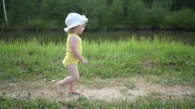 Sarışın, sevimli, bebek yaşta, sarı elbiseli, yaz gölünde yüzmeyi öğrenmekten korkan kız çocuğu. Artı vücut ölçüleri pozitif. Anne ve bebek doğal havuzda yüzüyor..