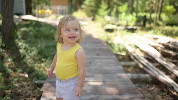 Mała zabawna blondynka dziecko maluch w żółtej podkoszulce i szare szorty spaceru bawiąc się na drewnianym eko szlaku na zewnątrz w lecie na przedniej wsi stoczni. Zdrowa koncepcja szczęśliwego dzieciństwa — Wideo stockowe