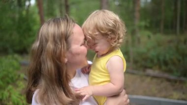 Annesinin kollarında bukleleri olan küçük tatlı bebek sarışın kız. Anne ve kızı yazın kırsal alanda ön bahçede birlikte vakit geçiriyorlar. Sağlıklı mutlu aile çocukluğu kavramı.