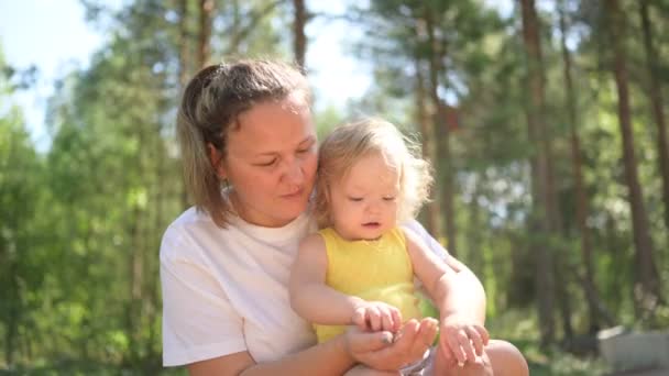 Petit bébé mignon tout-petit fille blonde avec des boucles sur les bras des mères. Mère et fille jouant passer du temps ensemble à l'extérieur à la campagne devant la cour été. Une famille heureuse saine concept d'enfance. — Video