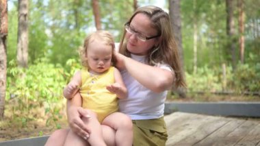 Annesinin kollarında bukleleri olan küçük tatlı bebek sarışın kız. Anne ve kızı yazın kırsal alanda ön bahçede birlikte vakit geçiriyorlar. Sağlıklı mutlu aile çocukluğu kavramı.