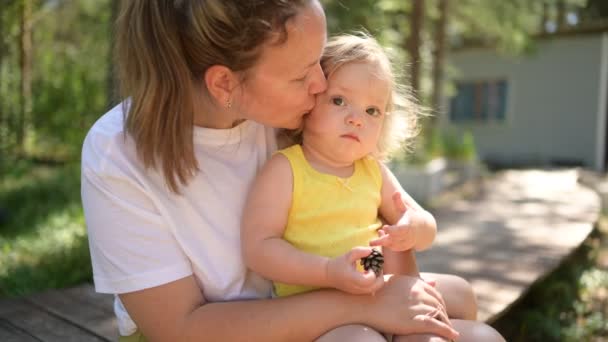 Petit bébé mignon tout-petit fille blonde avec des boucles sur les bras des mères. Mère et fille jouant passer du temps ensemble à l'extérieur à la campagne devant la cour été. Une famille heureuse saine concept d'enfance. — Video