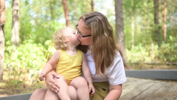 Petit bébé mignon tout-petit fille blonde avec des boucles sur les bras des mères. Mère et fille jouant passer du temps ensemble à l'extérieur à la campagne devant la cour été. Une famille heureuse saine concept d'enfance. — Video