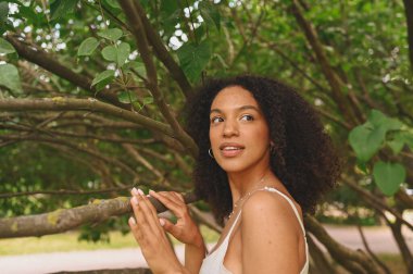 Şehvetli, çekici, doğuştan güzel, afro saçlı, yeşil yapraklı doğa parkında poz veren Afro-Amerikan kadının yakın moda portresi..