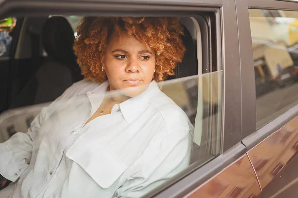 Jovem feliz sorrindo Africano americano mulher vermelho afro motorista de cabelos sentados em novo carro marrom, sorrindo olhando para a câmera desfrutando viagem. Cursos de condução e seguro de vida — Fotografia de Stock