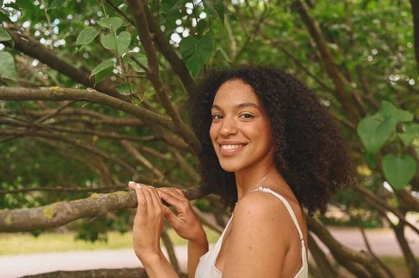 Fashion close up portrait of laughing atrakted young natural beautiful African American woman with afro hair and perfect toys approves posing in nature parkland in green foliage. — Stok Foto