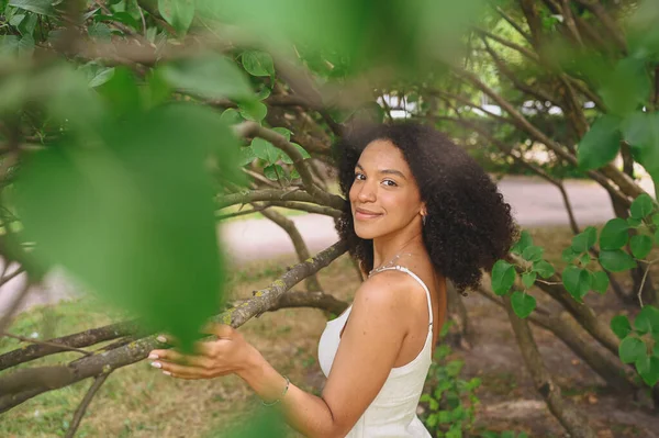 แฟชั่น close up รูปภาพของสาวสวยสาวสวยแอฟริกันอเมริกันธรรมชาติที่มีผม afro โพสในสวนธรรมชาติในใบไม้สีเขียว . — ภาพถ่ายสต็อก