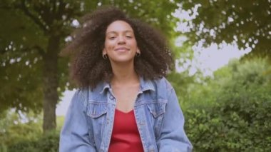 Şehvetli, çekici, doğuştan güzel, siyah saçlı, kot ceketli, kırmızı elbiseli, yaz aylarında yeşil doğa parkında yürüyen Afro-Amerikan kadının yavaş çekim portresi..
