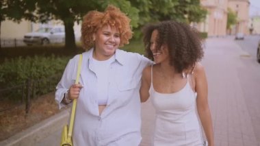 Güzel, mutlu, lezbiyen, Afro-Amerikan çift yazın şehir sokaklarında sarılıp geziyorlar. LGBT toplum konsepti. Bayan arkadaşlar gülümsüyor, birlikte aşk anlarının tadını çıkarıyorlar.