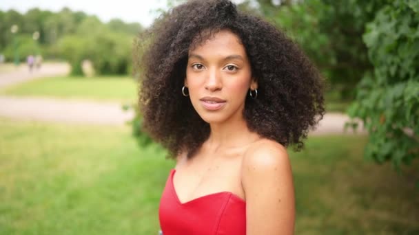 Moda de cerca retrato en cámara lenta de sensual atractiva joven naturalmente hermosa mujer afroamericana en corsé rojo con pelo afro posando en el parque natural en follaje verde. — Vídeos de Stock