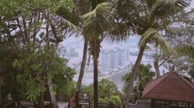 Luhuitou parkından Hainanların Sanya Şehri 'nin en iyi manzarası, yerel evler, lüks oteller ve binalar. Asya 'da yaz tatili cenneti. Kasvetli fırtınalı hava, rüzgarda sallanan palmiye ağaçları.