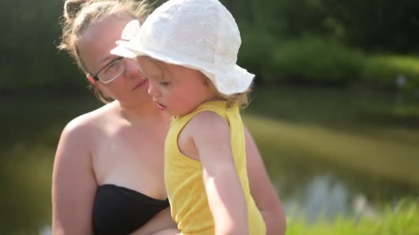 Petit bébé mignon tout-petit fille blonde avec des boucles sur les bras des mères. Mère et fille jouant passer du temps ensemble à l'extérieur à la campagne devant la cour été. Une famille heureuse saine concept d'enfance. — Video