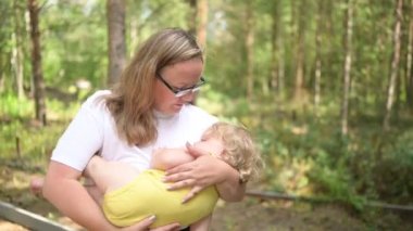 Annesinin kollarında bukleleri olan küçük tatlı bebek sarışın kız. Anne, yazları kızını kırsal alanda uyusun diye sallıyor. Sağlıklı mutlu aile çocukluğu kavramı.
