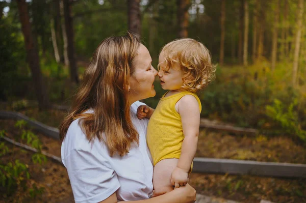 Kecil lucu bayi gadis pirang dengan ikal di lengan ibu. Ibu dan anak bermain menghabiskan waktu bersama-sama di luar ruangan di halaman depan pedesaan musim panas. Konsep masa kecil keluarga bahagia yang sehat. — Stok Foto