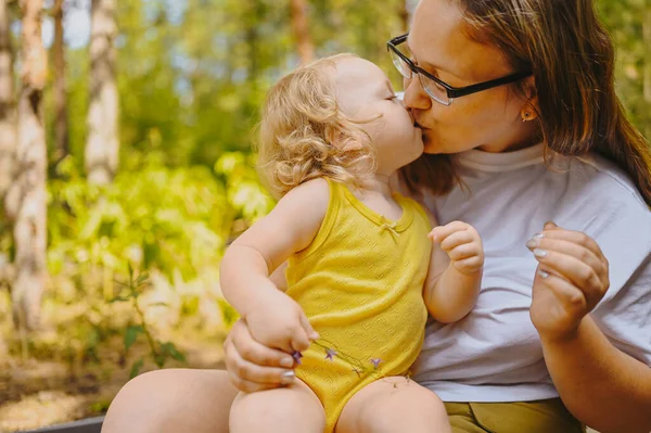 Kecil lucu bayi gadis pirang dengan ikal di lengan ibu. Ibu dan anak berciuman saat bermain bersama di luar ruangan di halaman depan saat musim panas. Konsep masa kecil keluarga bahagia yang sehat. — Stok Foto