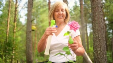 Yaşlı, kıdemli bahçıvan kadın, kır bahçesinde çiçeklere bakan kırsal alanda, su tozu kullanarak çiçek açan bitkileri ilaçlıyor. Çiftçilik, bahçıvanlık, tarım, emekli yaşlılar..