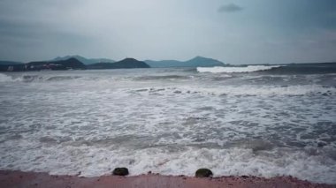 Sanya, Hainan 'da büyük ve modern bir sahil kasabası. Gökdelenleri var. Rüzgarlı ve fırtınalı havada, depresif su renklerinde dalgalar sörf yapar. Kasvetli deniz ya da okyanus .