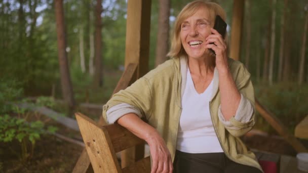 Tecnología, concepto de personas de edad avanzada ancianos anciano feliz sonriente mujer habla teléfono celular teléfono inteligente al aire libre en la terraza de madera en el patio trasero jardín de verano campo — Vídeos de Stock