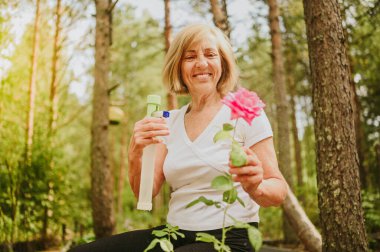 Yaşlı, kıdemli bahçıvan kadın, kır bahçesinde çiçeklere bakan kırsal alanda, su tozu kullanarak çiçek açan bitkileri ilaçlıyor. Çiftçilik, bahçıvanlık, tarım, emekli yaşlılar..