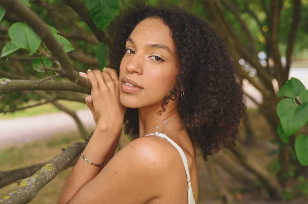 Fashion close up portrait of sensual atraktif muda alami indah wanita Afrika Amerika dengan rambut afro berpose di alam taman di dedaunan hijau. — Stok Foto