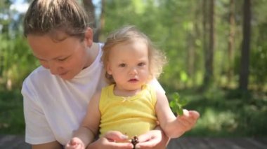 Annesinin kollarında bukleleri olan küçük tatlı bebek sarışın kız. Anne ve kızı yazın kırsal alanda ön bahçede birlikte vakit geçiriyorlar. Sağlıklı mutlu aile çocukluğu kavramı.