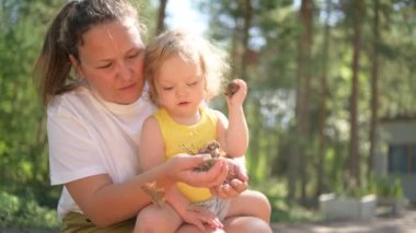 Annesinin kollarında bukleleri olan küçük tatlı bebek sarışın kız. Anne ve kızı yazın kırsal alanda ön bahçede birlikte vakit geçiriyorlar. Sağlıklı mutlu aile çocukluğu kavramı.