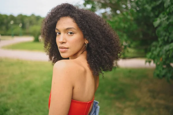 Potret mode menarik wanita muda Afrika Amerika yang cantik secara alami dengan rambut hitam afro dalam gaun korset merah berpose di taman alam dalam dedaunan hijau. — Stok Foto