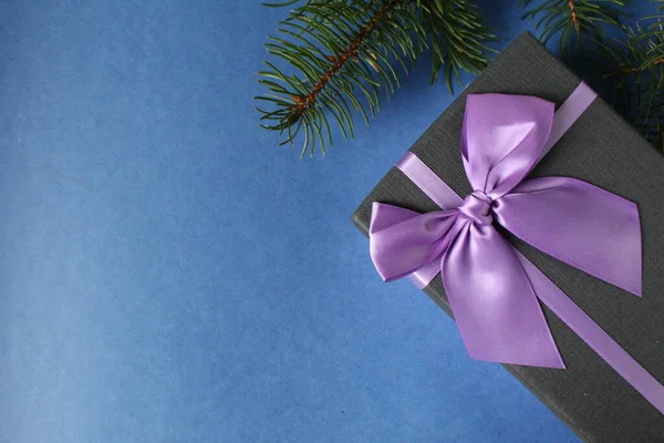 Yılbaşı arkaplan hediye paketi mor eflatun fuşya kurdelesi ve ladin çam ağaçlarından oluşan dallı mavi bir zemin üzerinde metin kopyalama alanı için yer olan.