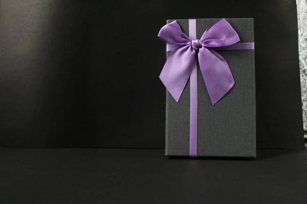 only black black gift gift box with purple lilac fuchsia ribbon and bow on a black background with space for text copy space father\'s day new year Christmas birthday for men