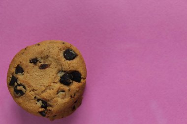 Çikolata damlalı kurabiyeler fotokopi alanının pembe arka planında üst üste dizilmiştir.