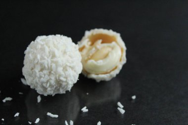 Bir iki üç hindistan cevizi serpiştirilmiş beyaz şekerler. Raffaello gibi parlak siyah bir arka planda yansıması olan bir kaç beyaz şeker. Metin için bir kopya alanı var.