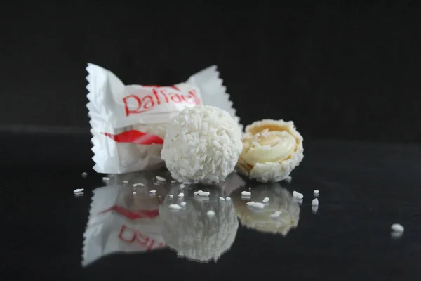 Şeker beyaz ve Raffaello, ürünün metni için fotokopi uzayından yansıyan siyah parlak bir arka planda yan yana uzanıyorlar.