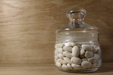 Parlak ahşap kapaklı cam bir kavanozda beyaz fasulyeler var..
