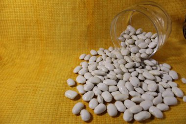 Kavanozdaki beyaz kuru fasulyeler sarı bir limon arkaplanına dökülmüş..