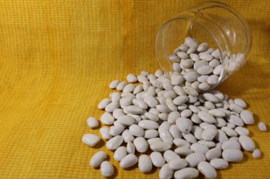 Kavanozdaki beyaz kuru fasulyeler sarı bir limon arkaplanına dökülmüş..