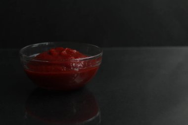 Siyah arka plan fotokopi alanı üzerine cam bir sos kasesine kırmızı domates sosu yapıştırıcısı..