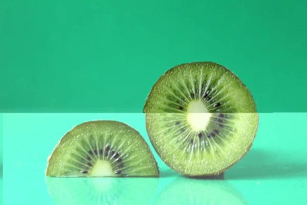 half and a circle of kiwi kusrchek with reflection on a green background with a copyspace.