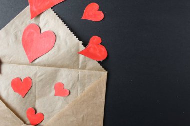 Kırmızı kalpler, el yapımı kahverengi zarftan siyah arka planda uzayın bir kopyasıyla birlikte çıkarlar..