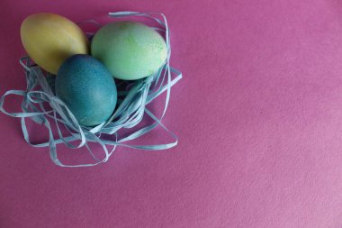 Paskalya arkaplanında üç tane çok renkli yumurta pembe arka planda metinler için yeri olan şekerdir..