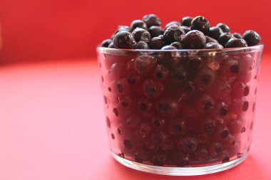 Kırmızı zemin üzerinde kırmızı bir bardakta böğürtlen ve üzümlü yaban mersini ya da üzümlü üzümlü sandviç..