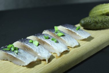 Tahta bir tahtanın üzerinde balık parçaları soğan yeşillikleri ve siyah bir zemin üzerinde salatalık ve metin ve kopyalama alanı olan bir yer..