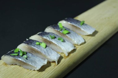 Tahta bir tahtanın üzerinde balık parçaları soğan yeşillikleri ve siyah bir zemin üzerinde salatalık ve metin ve kopyalama alanı olan bir yer..