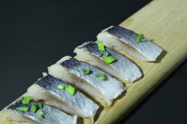 Tahta bir tahtanın üzerinde balık parçaları soğan yeşillikleri ve siyah bir zemin üzerinde salatalık ve metin ve kopyalama alanı olan bir yer..