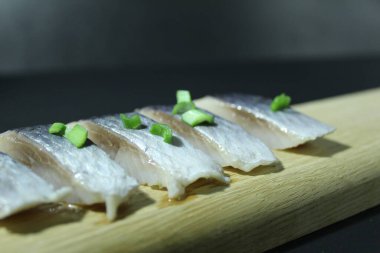 Tahta bir tahtanın üzerinde balık parçaları soğan yeşillikleri ve siyah bir zemin üzerinde salatalık ve metin ve kopyalama alanı olan bir yer..