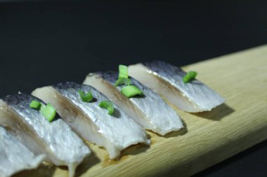 Tahta bir tahtanın üzerinde balık parçaları soğan yeşillikleri ve siyah bir zemin üzerinde salatalık ve metin ve kopyalama alanı olan bir yer..