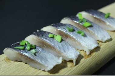 Tahta bir tahtanın üzerinde balık parçaları soğan yeşillikleri ve siyah bir zemin üzerinde salatalık ve metin ve kopyalama alanı olan bir yer..