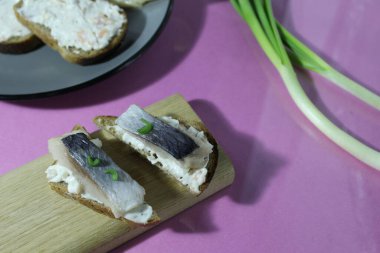 Çerez sakuska soğuk sandviç kanepesi, ringa balıklı ekmek, ahşap üzerinde, leylak rengi mor arka planda soğanın yanında..