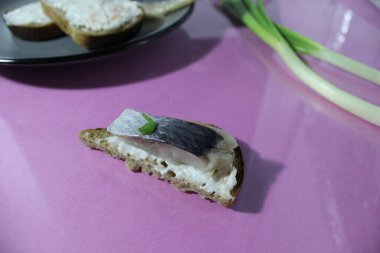 Tuzlu ringa balıklı bir kanape sandviçi ve eflatun arkaplanda yeşil soğanın yanında ekmek..