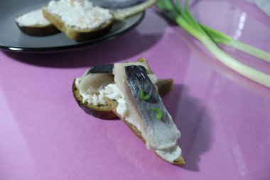 Tuzlu ringa balıklı bir kanape sandviçi ve eflatun arkaplanda yeşil soğanın yanında ekmek..